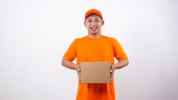 Asian deliveryman in orange t-shirt uniform holding a package box parcel isolated on white background photo
