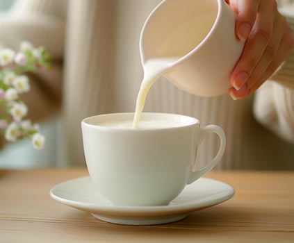 Person pouring milk into a white cup photo