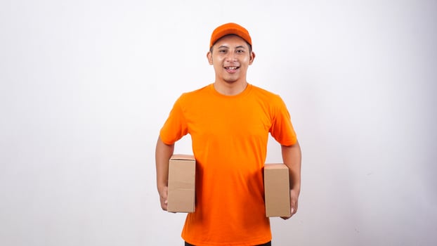 Asian deliveryman in orange t-shirt uniform carrying package boxes parcel on his both sides isolated on white background photo