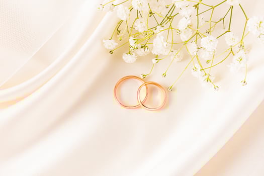 Two gold wedding rings lie on a beautiful satin background of beige tone, with delicate waves of fabric and a sprig of white gypsophila. postcard. photo