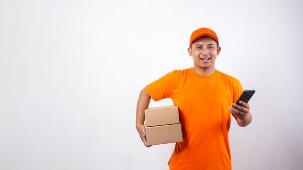 Asian Delivery man in orange t-shirt carrying package boxes parcel while holding a smartphone isolated on white background photo