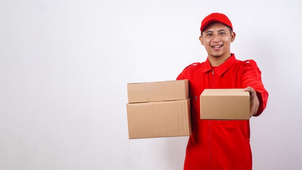 Delivery man in red uniform carrying package boxes and giving other package box to customer isolated on white background photo