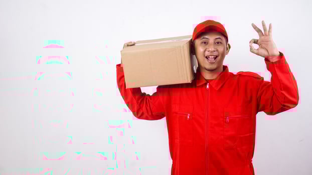 Delivery man in red uniform carrying stack of package box parcel on his shoulder and showing okay sign with his fingers isolated on white background photo