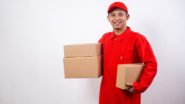 Smiling Asian Delivery man in red uniform carrying package boxes parcel isolated on white background photo