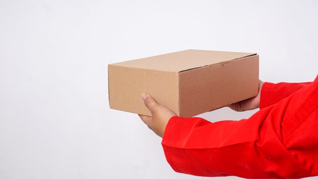 Close up of delivery man in red uniform deliver a package box parcel to customer isolated on white background photo
