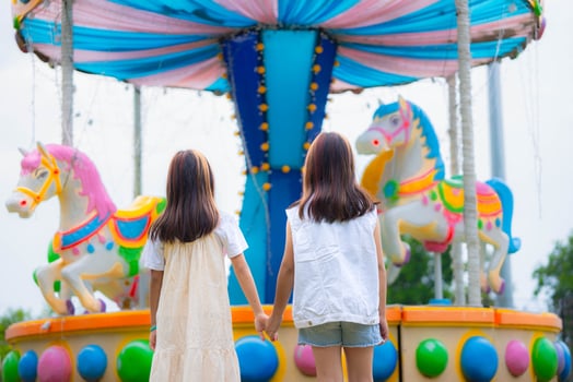 Rear view of two Asian girls holding hands and laughing as they walk through a colorful amusement park. photo