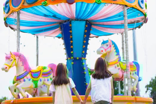 Rear view of two Asian girls holding hands and laughing as they walk through a colorful amusement park photo