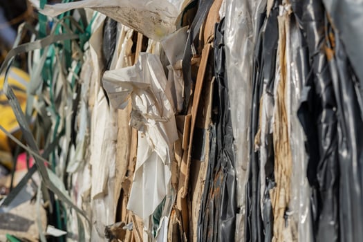 Large bales of compressed plastic waste sit tightly packed at a recycling facility under clear blue skies, reflecting sustainability efforts photo