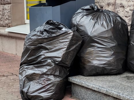 Two large black garbage bags rest against a stone ledge near a building, showcasing urban waste disposal habits photo