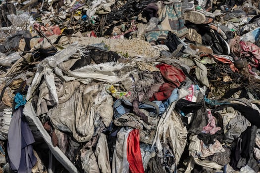 A vast pile of discarded clothes and textiles accumulates at a landfill under bright sun, showcasing the issue of waste management photo