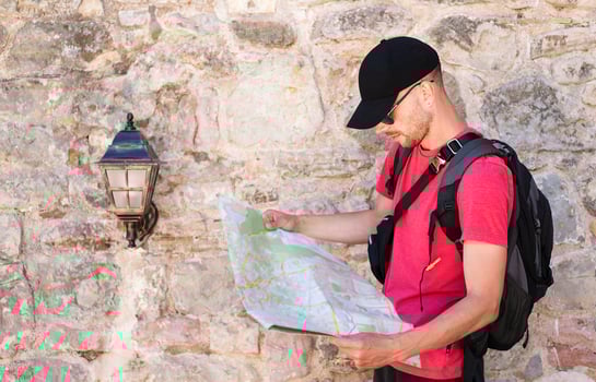Young man tourist in a cap and with a backpack stands in the old town and looks at the tourist map. Man visiting the sights in the old town. Selective focus. photo