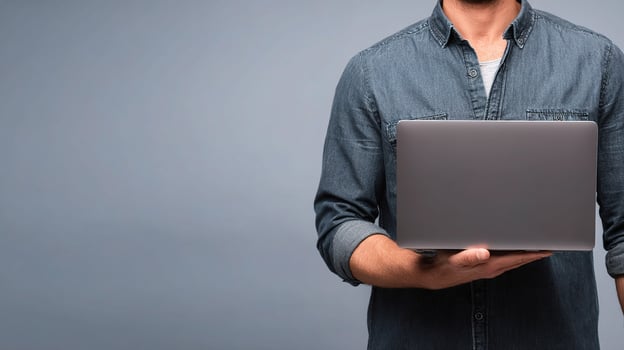 A man in a denim shirt holding a laptop photo