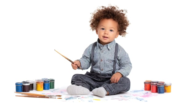 A toddler sitting on the floor with paint brushes and paints photo
