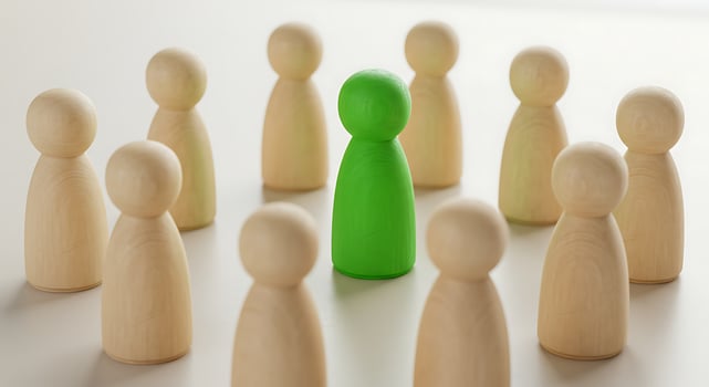 Green Peg Doll Stands Out Among Beige Wooden Figures photo