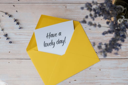 HAVE A LOVELY DAY text on supportive message paper note reminder from yellow envelope. Flat lay composition dry lavender flowers. Concept of inner happiness, slowing-down digital detox personal fulfillment. Top view photo
