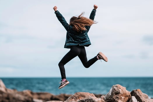 A woman jumping on rocks near the ocean photo