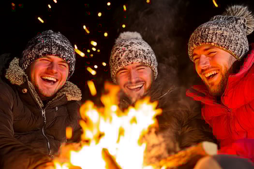 Three men in winter clothing sitting around a campfire photo