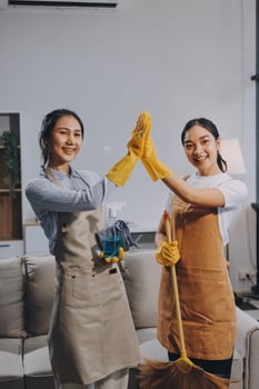 Two women in aprons holding a broom and giving high five photo