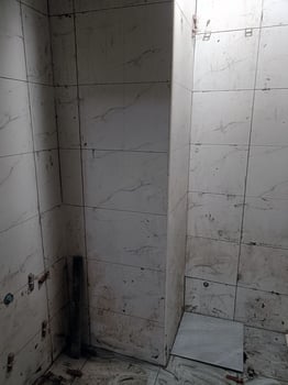 Bathroom corner with white tile and drain shows worn, unkempt state of being as grout is dirty and floor is stained, creating feeling of neglect photo