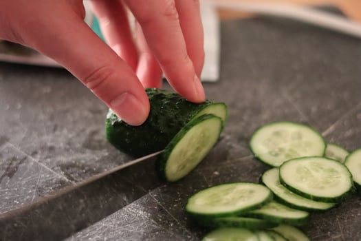 Chopping fresh cucumber into slices on a cutting board in a cozy kitchen during daylight hours photo