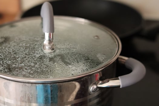 Cooking a pot of water on a stovetop with steam forming under the lid in a kitchen setting photo