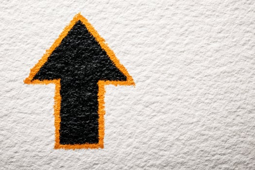 A black arrow symbol, outlined in orange, points upwards on a textured white background. The contrast between the dark arrow and the light surface creates a striking visual effect. photo