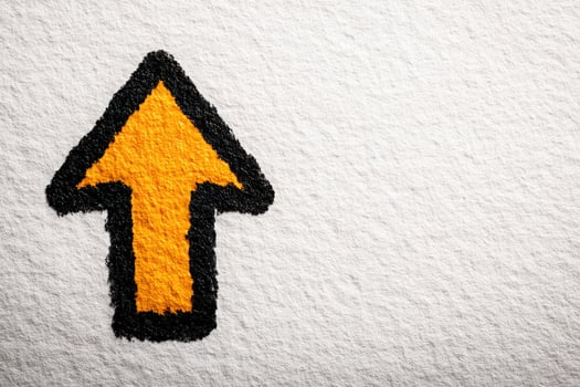 A bold orange arrow outlined in black is depicted on a textured white surface, effectively directing attention upwards. The vibrant colors contrast sharply, providing a clear visual cue. photo