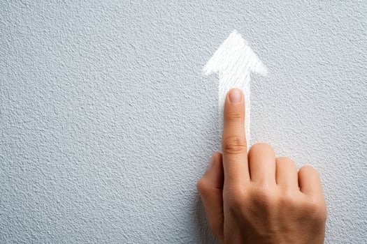 A hand with a finger extended points towards a white arrow sketch on a gray wall. The gesture suggests direction or an upward movement, creating an engaging visual focus. photo