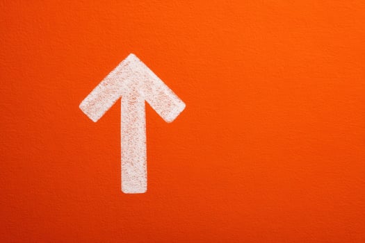 A large white arrow is painted on a vibrant orange wall, directing attention upwards. This striking design element enhances the visual appeal and guides viewers focus. photo