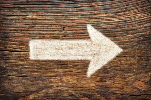 A weathered wooden surface features a white painted arrow pointing to the right. The texture of the wood is rustic, enhancing the arrows visibility and purpose. photo