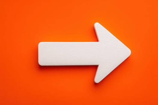 A white arrow pointing right is placed on a bright orange surface. This design is ideal for signage or directional guidance. The contrast creates an eye-catching visual appeal. photo
