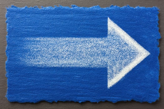 A vibrant blue rectangular surface features a large, white arrow on the right side, suggesting direction. The arrow appears drawn with a fine texture, enhancing visibility and clarity. photo