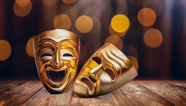 Two golden theatrical masks, one depicting comedy with a wide smile, the other tragedy with a downturned mouth, resting on a wooden surface with blurred golden bokeh lights in the background. photo