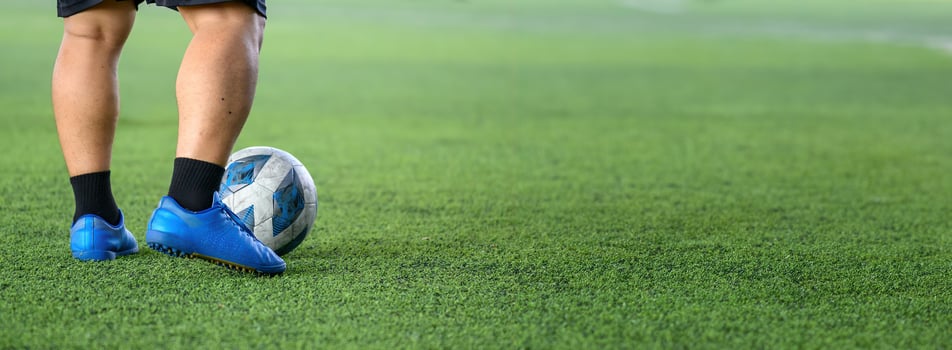 Soccer player standing on green grass field with blue cleats and black socks, focusing on ball near feet during game or practice session photo