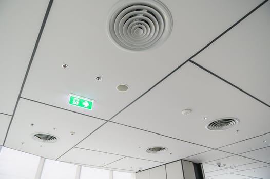 Clean modern office ceiling featuring air vents, recessed lighting, and grid pattern with emergency exit sign glowing green, creating bright and organized atmosphere photo