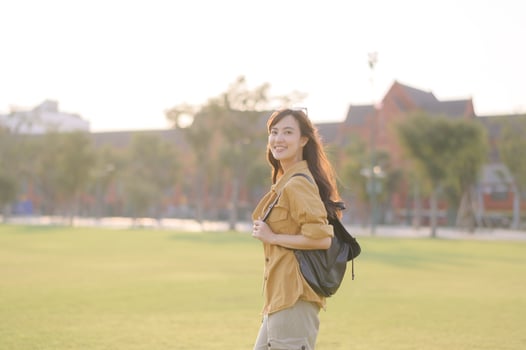 Asian woman traveler with backpack smiling in sunlight, enjoying outdoor adventure in city park, summer holiday vacation in Bangkok photo