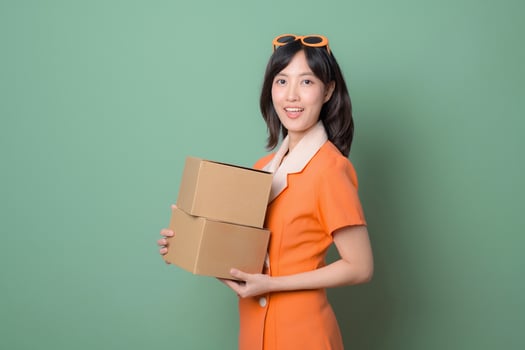 Cheerful woman in orange dress holds cardboard boxes against green background, ready for delivery or moving, expressing happiness photo