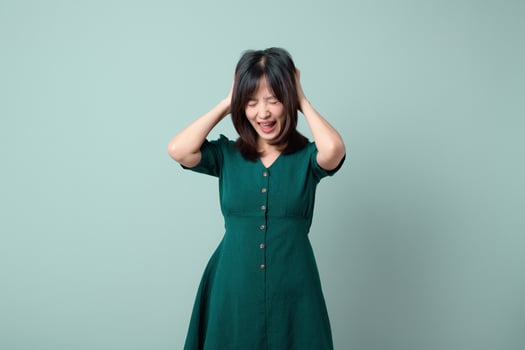 Asian woman green dress hands on head emotional closed eyes green background stress frustration photo