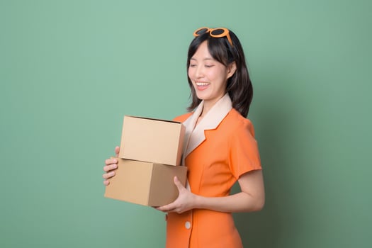 Southeast asian woman holding cardboard boxes with happy expression represents internet online shopping and delivery service against green background photo