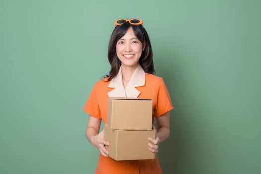 Southeast asian woman in orange dress holding cardboard boxes smiling against green background delivery concept photo
