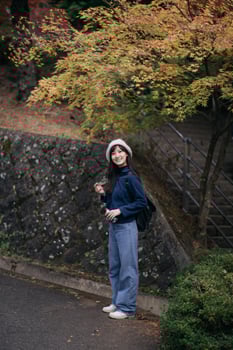 Southeast Asian woman travel in autumn park wearing casual clothes and hat smiling happily near colorful tree with backpack enjoying outdoor nature photo