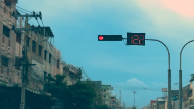 Red traffic lights both LED and digital hang from curved steel poles. Blurred images of large city buildings stand tall on both sides. Under the sky. photo