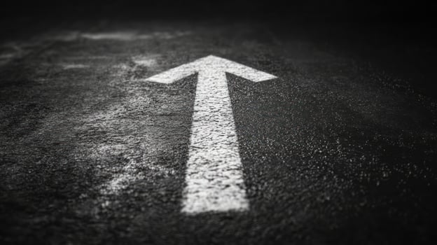 White arrow painted on dark asphalt road surface pointing forward symbolizing direction and progress in minimalistic style photo