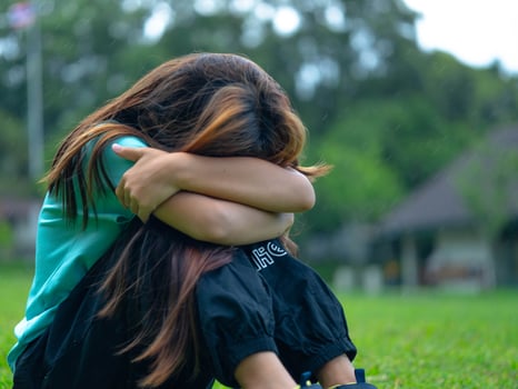 Unhappy sad little girl sitting alone hugging her knees in the park. photo