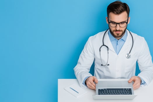 A male doctor in a white coat is working on his laptop photo