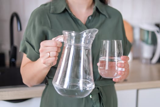 woman holding a pitcher in a glass with water in the kitchen water helps to increase hydration levels and improve metabolism concept of healthy lifestyle, cooking blogs. photo