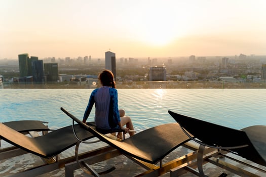 Woman sitting by rooftop infinity pool at sunset, enjoying peaceful view of city skyline with warm sunlight reflecting on the water in a serene urban setting photo
