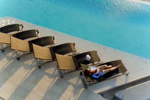 Aerial view of young woman sunbathing alone on a lounge chair by a rooftop infinity pool with sparkling water, enjoying summer sunlight and peaceful moment photo