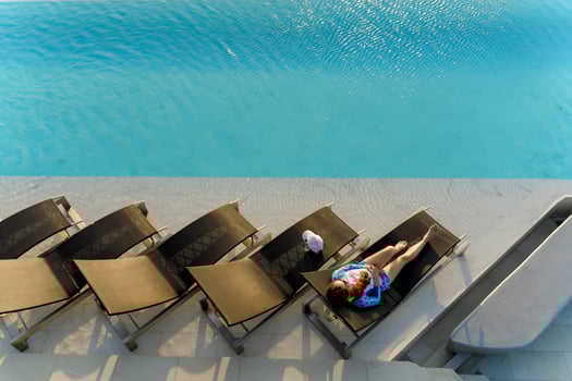 Top view of young woman relaxing alone on a lounge chair by rooftop infinity pool in bright sunlight, enjoying peaceful summer moment and clear blue water photo