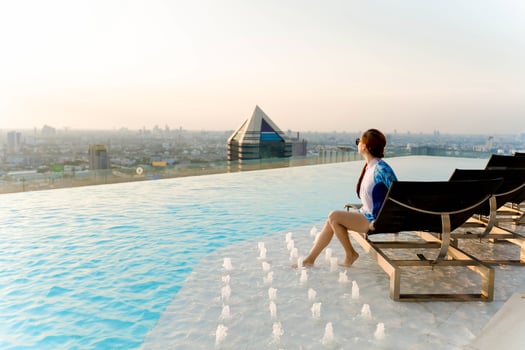 Woman relaxing at a rooftop infinity pool with foot fountains, enjoying panoramic city skyline view and soft sunlight in a peaceful urban escape photo